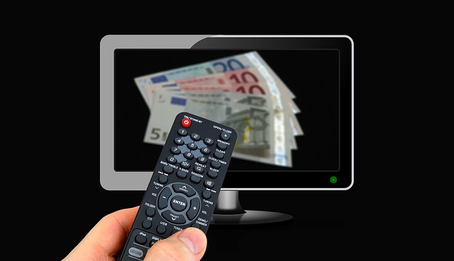 Ruka drží ovladač, v dáli televize.